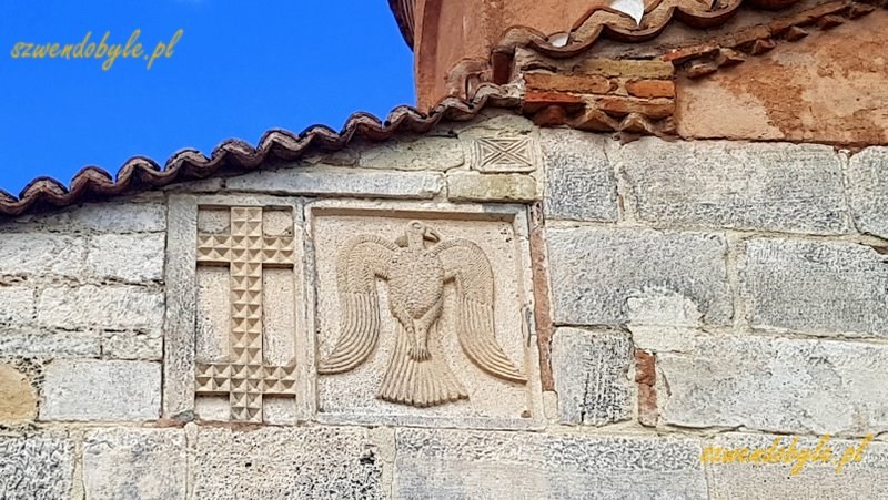 Albania, Apollonia Iliryjska. Fragment muru kościoła, do budowy wykorzystano bloki kamienne ze starożytnych budowli. Detal - na jednym z kamieni widać wyrzeźbionego orła. Obok niego płaskorzeźba krzyża z dwiema poziomymi belkami równej długości. 20240504_144427-ink