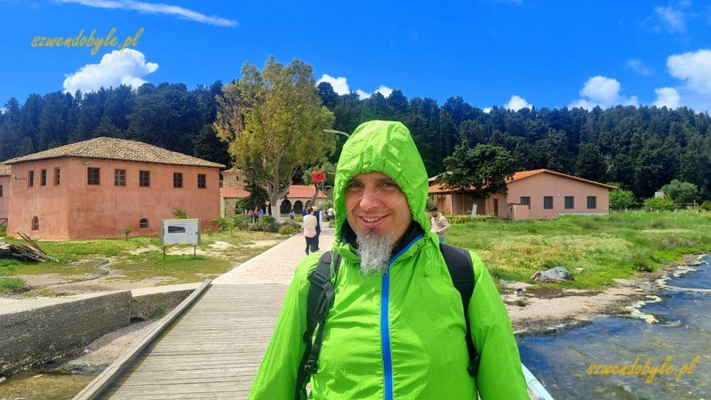Albania, Zvernec. Jarek w zielonej kurtce z kapturem stoi na moście. Z tyłu widać zabudowania klasztoru. 20240504_124820-ink