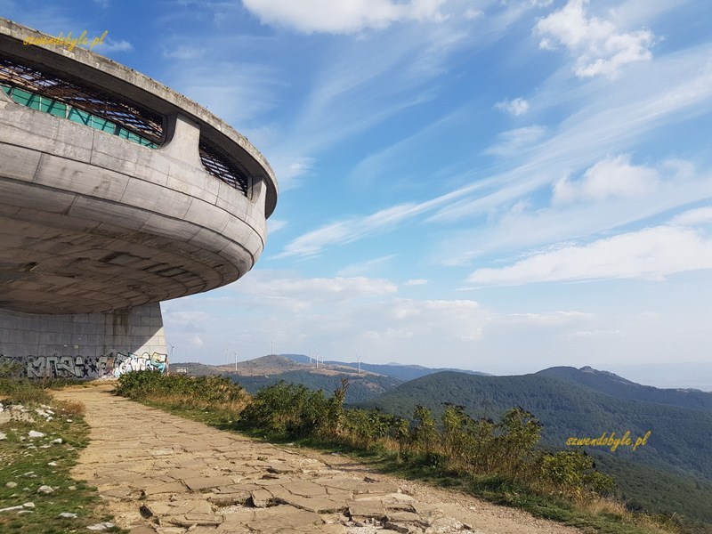 Buzłudża, po lewej stronie fragment "betonowego UFO", po prawej kamienna ścieżka i panorama gór.