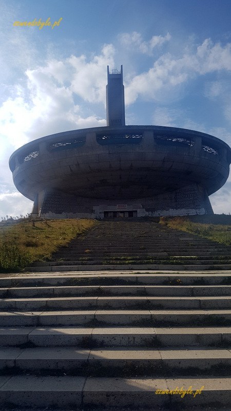 Buzłudża, widok na monumentalny budynek wraz z prowadzącymi do wejścia schodami. Zdjęcie od strony oficjalnego parkingu. Nad budynkiem góruje wieża, niczym dzwonnica kościelna.