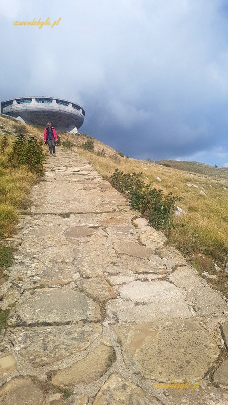 Buzłudża, strome zejście ścieżką brukowaną płaskimi kamieniami. W tle "betonowe UFO" na szczycie góry.