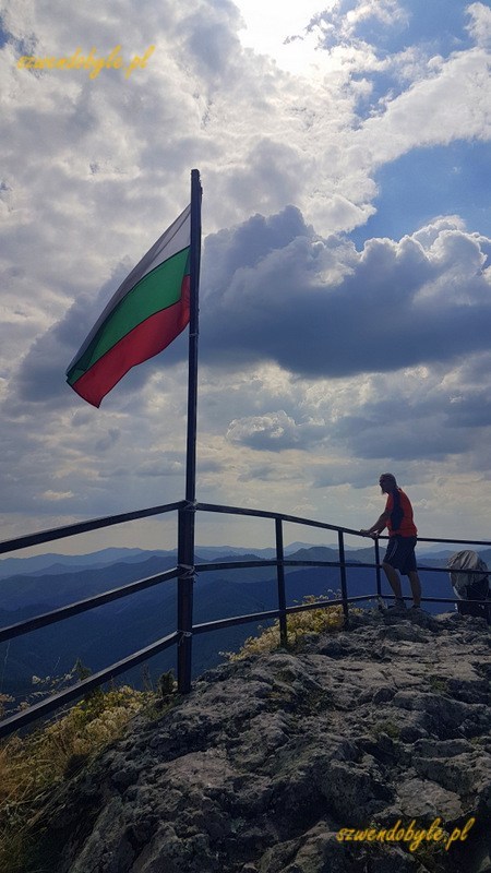 Momcziłowa twierdza - widok na Rodopy. Flaga bułgarska powiewa na szczycie wzniesienia. Jarek w tle, w odległości kilku metrów za flagą. 20231001_113446-ink