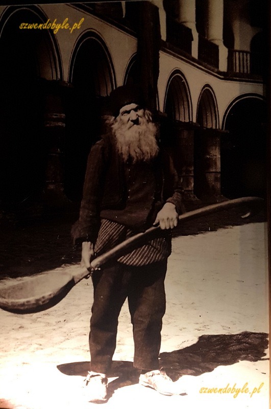 Monastyr Rilski, zdjęcie fotografii prezentowanej w muzeum - na dziedzincu, na tle krużganków stoi brodaty mężczyzna, oburącz trzyma wielką drewnianą łyżkę, której długość jest porównywalna z jego wzrostem. 20231005_110729-ink