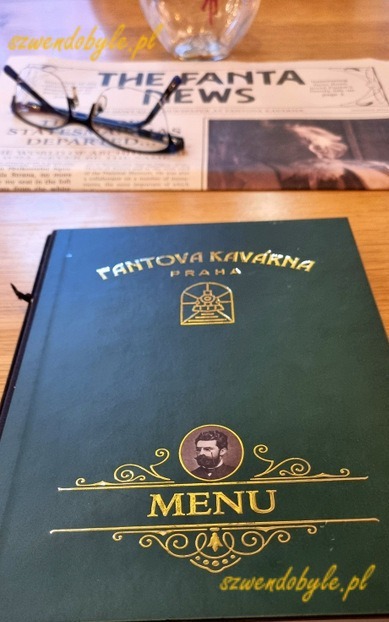Praga dworzec gł&oacute;wny - Praha hlavn&iacute; n&aacute;draž&iacute; - zielona okładka menu w kawiarni w zabytkowym budunku dworca, powyżej gazeta stylizowana na starą i okulary. 20241111_144645-ink