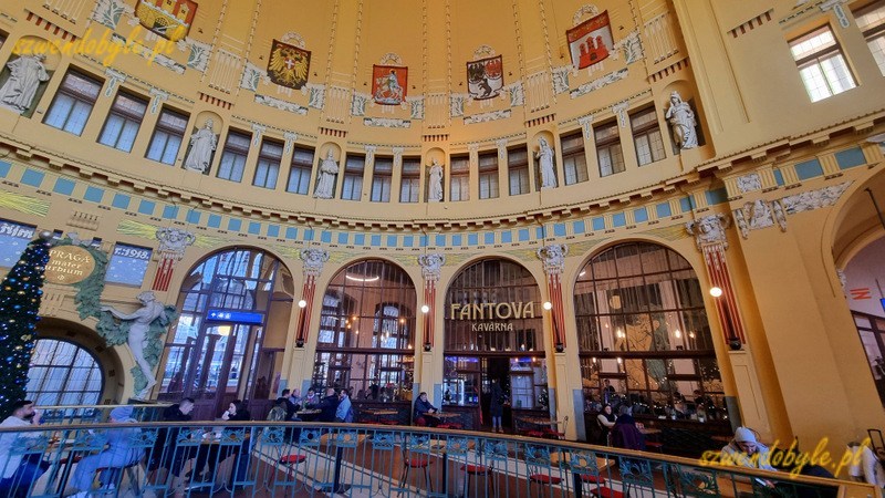 Praga dworzec gł&oacute;wny - Praha hlavn&iacute; n&aacute;draž&iacute; - kopuła w holu zabytkowego budynku dworca, dookoła namalowane herby. Na wprost,nieco po prawej wejście do kawiarni. 20251228_143943-ink