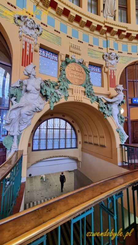 Praga dworzec gł&oacute;wny - Praha hlavn&iacute; n&aacute;draž&iacute; - zdjęcie w holu zabytkowego budynku dworca, na wrost łaciński napis "Praga mater urbium", poniżej widać tunel prowadzący z nowego dworca na perony. 20251228_144042-ink