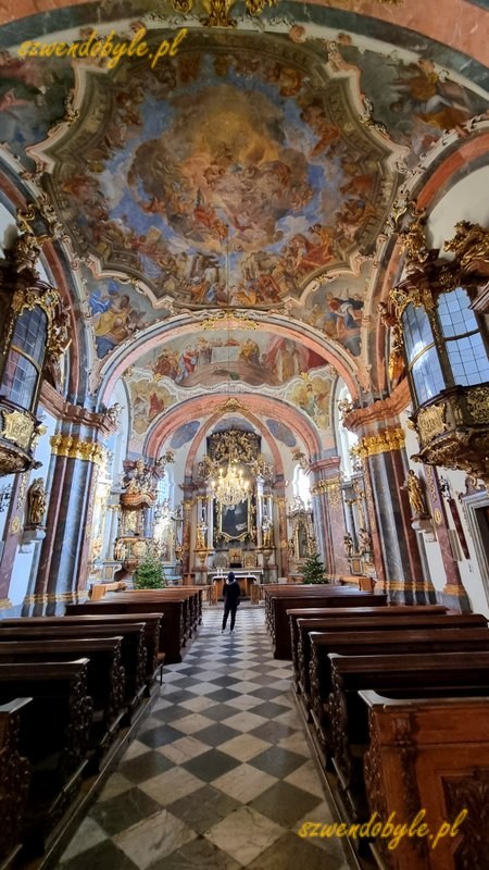Praga, Loreta czyli kompleks pielgrzymkowy epoki baroku. Widok na ołtarz, pośrodku jedna osoba stoi przed ołtarzem. Po bokach widać 2 przeszklone barokowe balkony umieszczone powyżej drzwi bocznych. 20251226_110544-ink