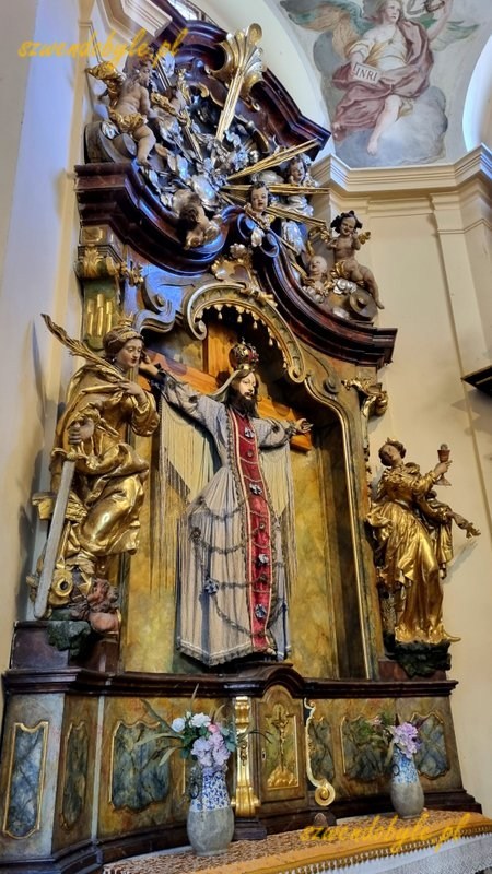 Praga, Loreta czyli kompleks pielgrzymkowy epoki baroku. Ołtarz - na krzyżu wisi Wilgefortis, kobieta z brodą i koroną na głowie. Ołtarz w arkadach na dziedzińcu. 20251226_110902-ink