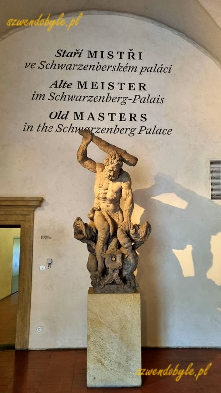 Czechy,Praga. Pałac Schwarzenberg&oacute;w. Rzeźba przedstawiającap&oacute;łnagiego mężczyznę z maczugą w ręce. Powyżej na ścianie napis "Starzy mistrzowie w Pałacu Schwarzenberg&oacute;w" po czesku, niemiecku i angielsku. 20251226_130343-ink