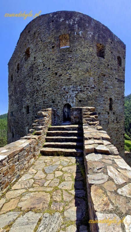 Zamek Velhartice, Czechy. Widok z kamiennego mostu w kierunku wieży mieszkalnej (Rajski Dom). Na końcu mostu kilka kamiennych schodków w górę, za nimi drewniany pomost łączący wieżę i most. 20250620_123835-ink
