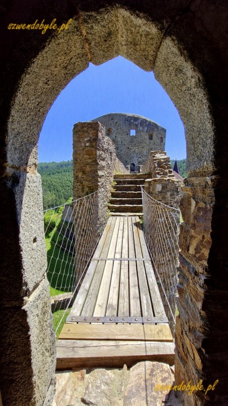 Zamek Velhartice, Czechy. Widok na górny poziom kamiennego mostu przez drzwi w wieży ostatniej obrony (donżon). Na końcu drogi wieża mieszkalna (Rajski Dom). Na pierwszym planie, zaraz za drzwiami drewniany pomost pomiędzy donżonem i mostem. 20250620_123955-ink