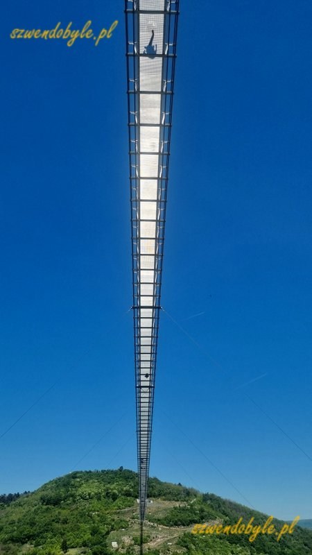 Węgry, Zemplén 723 - wiszący Most Jedności Narodowej. Widok z dołu, most na tle bezchmurnego nieba, widać cienie ludzi idących mostem. 20260503_125325-ink
