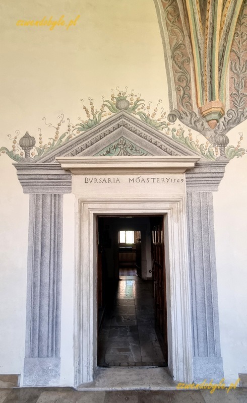 Kraków, opactwo cystersów w Mogile. Kamienny portal drzwi, w jego górnej części napis "Bursaria moastery 1569". Wokół kamiennego portalu namalowany szerszy portal powiększa optycznie wejście. 20250615_124149-ink