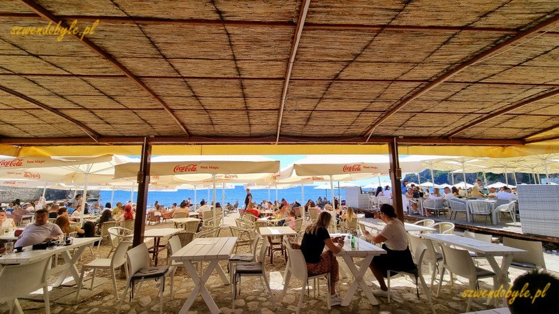 Czarnogóra, Budva. Stoliki baru na plaży pod słomianym zadaszeniem. 20250502_134402-ink