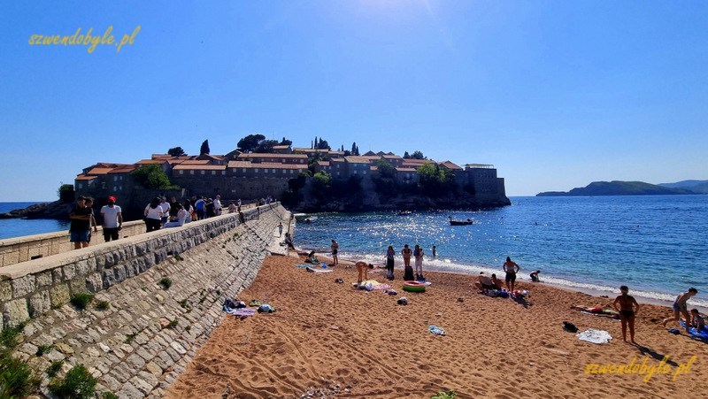 Czarnogóra, Sveti Stefan. Grobla prowadząca do dawnej twierdzy, na pierwszym planie fragment plaży. 20250502_155535-ink