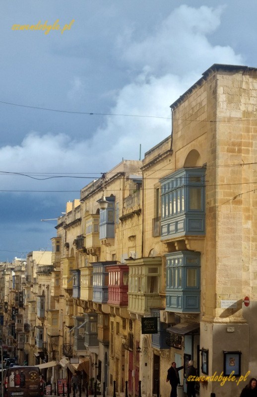 Maltańskie balkony, Valletta. Perspektywa ulicy schodzącej ostro w dół. Poprawej widać kamienice i wiele balkonów w różnych kolorach.