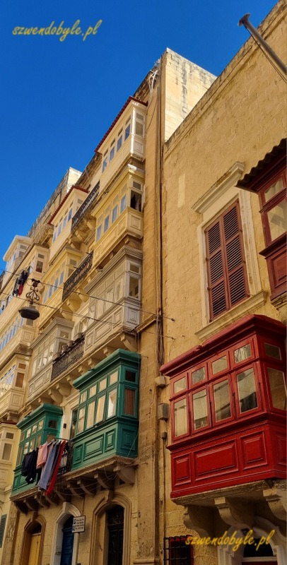 Balkony na Malcie, Valletta. Nagromadzenie kolorowych balkonów (czerwony, zielone) na ścianach kamienic. Na jednym z balkonów wywieszone pranie nad ulicą. 