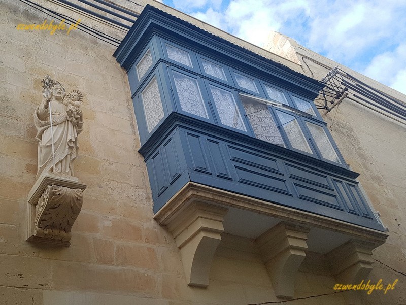 Malta, Valletta. Niebieski balkon, obok niego na ścianie kamienna figura świętego.