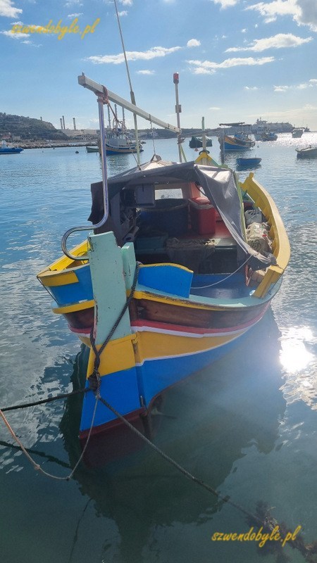 Malta, Marsaxlokk. Kolorowa łódź zacumowana w porcie. Słońce odbija się od wody.