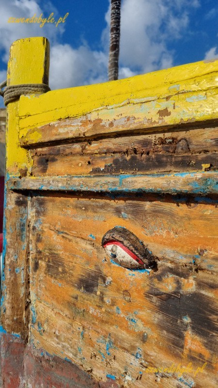 Malta, Marsaxlokk. Fragment burty łodzi oczekującej na remont. Z kolorów pozostał tyko żółty na górnej krawędzi burty. Oko łodzi również czeka na odmalowanie.