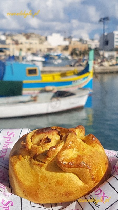 Malta, Marsaxlokk. Bułeczka na tle kolorowej łodzi. 