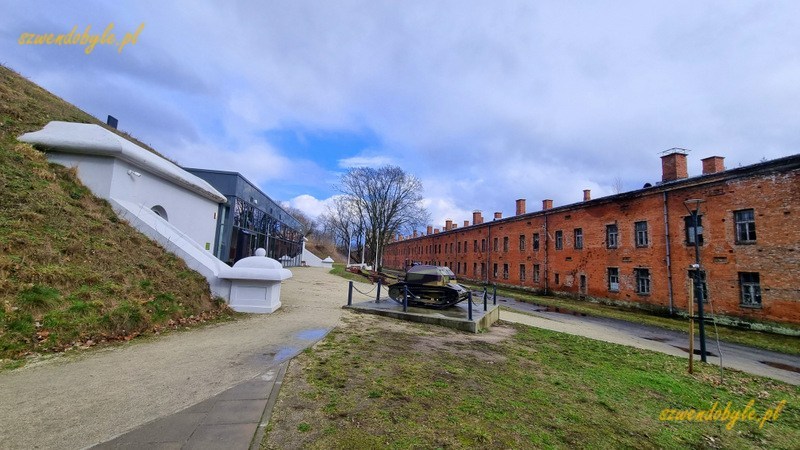 Modlin, widok na budynek koszar (po prawej) i Centrum Edukacji Historycznej Prochownia 197. Pośrodku niewielki zabytkowy pojazd pancerny.