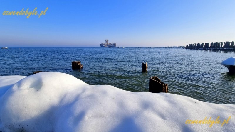 Gdynia, Babie Doły. Widok na pale wbite w dno morza. Pośrodku zdjęcia torpedownia. Na pierwszym planie śnieg. 20260228_091935-ink