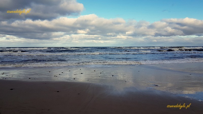 Hel, plaża. Na mokrym od wody morskiej piasku odbicia nieba i chmur.