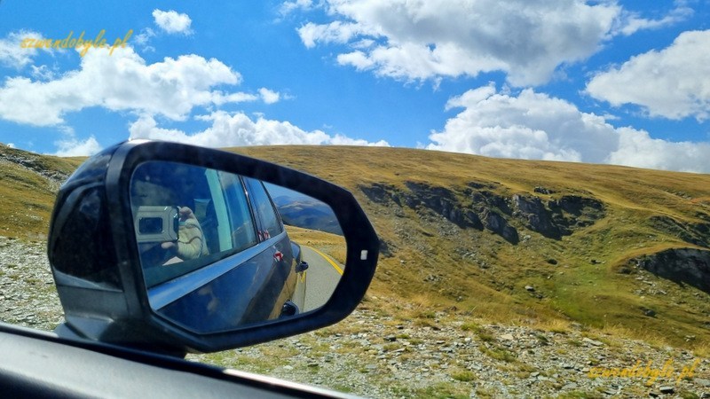 Rumunia, Transalpina. Na pierwszym planie lusterko boczne naszego auta. Widać odbicie telefonu. 20240908_131128-ink