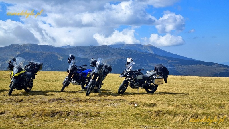 Rumunia, Transalpina. 4 motocykle zaparkowane na płaskiej ziemi porośniętej niską trawą. W tle widać oddalone góry. 20240908_133043-ink