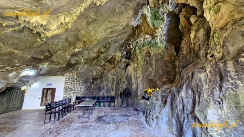 Wietnam, wyspa Cát Bà, jaskinia, w której mieścił się szpital wojskowy, czyli Military Hospital Cave. Wejście do jaskini przez metalowe drzwi w betonowej ścianie. Stół i krzesła dają możliwość odpoczynku po wspinaniu się schodami oraz wysłuchania przewodnika. 20251124_113828-ink