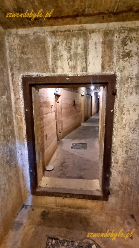 Wietnam, wyspa Cát Bà, jaskinia, w której mieścił się szpital wojskowy, czyli Military Hospital Cave. Betonowa ściana z niewielkim otworem na drzwi, za nim korytarz z betonowych ścian. 20251124_114209-ink