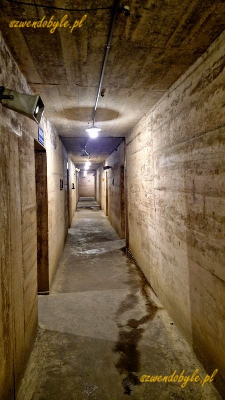 Wietnam, wyspa Cát Bà, jaskinia, w której mieścił się szpital wojskowy, czyli Military Hospital Cave.Betonowy korytarz, po bokach wejścia do pomieszczeń. Pod sufitem wisi megafon. 20251124_114300-ink