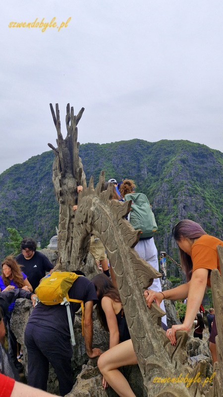 Wietnam, region Ninh Binh. Tłum ludzi mozolnie jeden za drugim idzie po ostrych kamieniach wzdłuż figury smoka na szczycie g&oacute;ry - w stronę jego głowy. 20251111_112649-ink