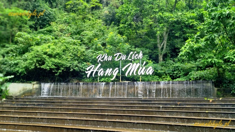Wietnam, region Ninh Binh. Na tle zieleni napis w języku wietnamskim "Hang Mua" (Jaskinia Mua) powyżej sztucznej kaskady wodnej w parku. 20251111_122254-ink