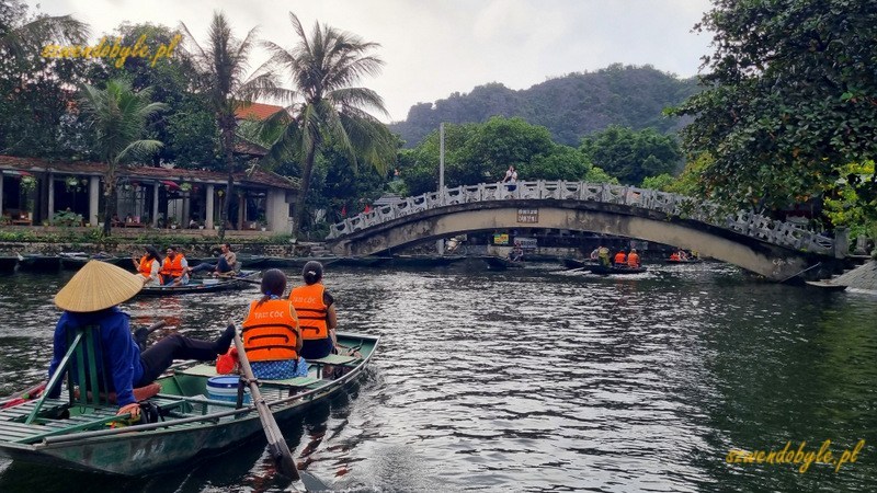 Tam Coc, Vietnam. Łodzie na rzece Ngo Dong płyną w kierunku jaskini. Wioślarka macha wiosłami z użyciem st&oacute;p. 20251110_151218-ink