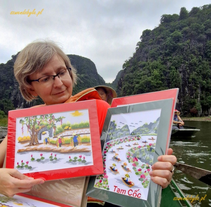Tam Coc, Vietnam. Karolina prezentuje wyszywane obrazy oferowane przez panią kierującą łodzią. 20251110_160525-ink